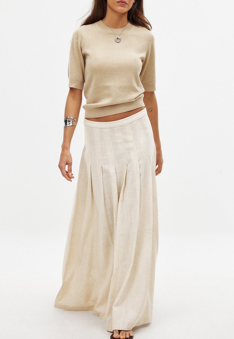 Top corto a maniche corte in maglia beige abbinato a una lunga gonna fluida color crema con pieghe verticali e una texture liscia.