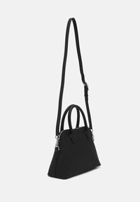 Sac à main synthétique noir avec une forme triangulaire structurée. Il dispose de deux poignées courtes et d'une longue bandoulière réglable avec des accents en métal argenté.