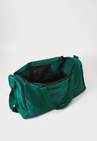 Grønn duffelbag med svarte detaljer, laget av slitesterkt materiale. Har doble håndtak, glidelås lukking, og et romslig indre.