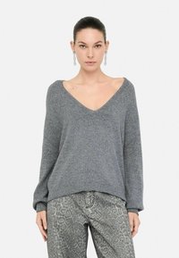 Pull en tricot gris avec un décolleté en V plongeant, coupe ample et manches côtelées. Associé à un jean gris à motifs avec une texture subtile.