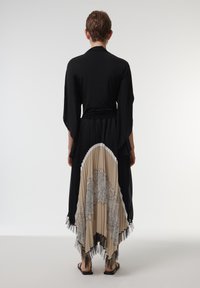 Blusa negra de manga larga combinada con una falda plisada asimétrica que presenta tela beige, un patrón de encaje y detalles de tul negro.