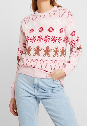 Lichtroze kersttrui met peperkoekmannetjes, candycanes, pepermuntwervelingen, hulst en de tekst "Vrolijk Kerstfeest", gedragen met lichtblauwe spijkerbroek.