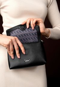 Černá kožená taška s texturovaným povrchem a stříbrným logem. Vnitřek má vzorované podšívku v šedé a modré barvě, uzavřenou na patentku.
