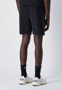 Pantaloni sportivi neri con cintura elastica, abbinati a calze nere a coste e sneaker bianche, mostrati dal retro.