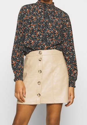 Blusa floreale nera con fiori arancioni e bianchi, colletto alto e maniche lunghe. Gonna mini in pelle beige con bottoni frontali e texture liscia.