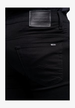 Mustardama denim püksid, millel on tekstuuriga nahklabel vöökohal ja peened õmblused tagakottidel.