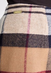 Jupe en laine à carreaux beige, marron et bleu marine. Elle présente une plaque de logo en or et une finition texturée avec un motif à carreaux classique.