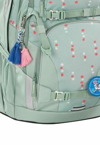Mint green backpack with a spotted pattern in red and white. Features include a side pocket, adjustable straps, and decorative tassels.