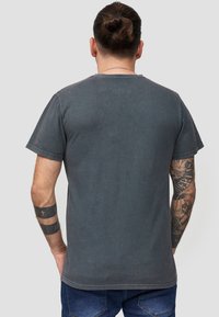 T-shirt grigia in cotone con maniche corte, scollatura rotonda e vestibilità rilassata. Il tessuto ha una leggera texture e un effetto di lavaggio sbiadito.