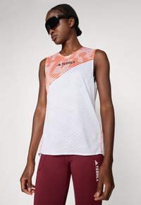 Débardeur de sport sans manches blanc avec des rayures orange et un motif texturé ; présente un col rond et un logo sur la poitrine.