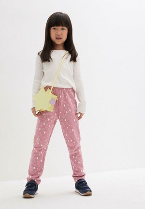 Leichtes weißes Langarmoberteil, rosa Hose mit elastischem Bund und weißem Tropfenmuster, marineblaue Sneakers und eine sternförmige gelbe Tasche.