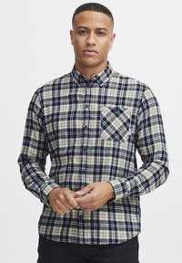 Rutete flanellskjorte i beige og marineblå; lange ermer, knappedesign, med en lomme med diagonalt mønster.