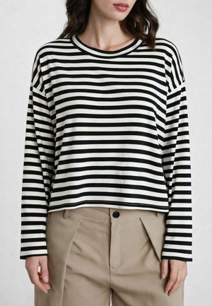 Donna che indossa un top a maniche lunghe a righe orizzontali bianche e nere con pantaloni beige a vita alta e piegheati.