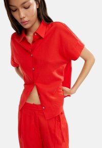Czerwona krótko-sleeve koszula na guziki wykonana z lekkiego materiału, charakteryzująca się luźnym krojem i widocznymi guzikami z przodu.