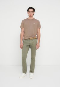 Καφέ βαμβακερό t-shirt, στρογγυλή λαιμόκοψη, κοντά μανίκια, συνδυασμένο με ελιάς πράσινα στενά παντελόνια και λευκά αθλητικά παπούτσια. Απλός σχεδιασμός, χωρίς ορατά μοτίβα.