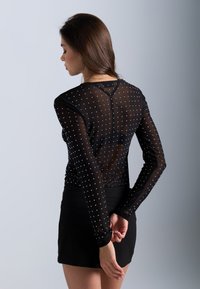 Svart, gjennomsiktig langermet topp med små sølvprikker, rund hals og slim fit, kombinert med et svart miniskjørt.