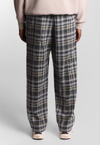 Pantalons à jambe large en plaid de couleur grise, noire et vert olive, en tissu doux avec une coupe décontractée et une finition lisse et texturée.