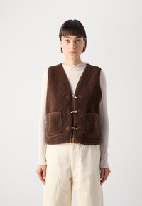 Brown, fleece vest with a textured surface, two front pockets, and brown trim. Fastened with three metallic clasps on a pointed flap design.