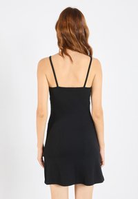 Musta hihaton mekko, jossa on istuva bodice ja levenevä helma, valmistettu joustavasta, ribatusta kankaasta ja kapenevista olkaimista.