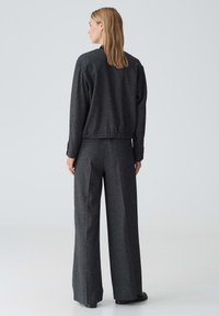 Graham, strukturiertes Strickjackett mit tailliertem Schnitt und langen Ärmeln, kombiniert mit lockeren, weit geschnittenen Hosen aus passendem Stoff.