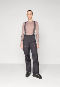 Black waterproof ski pants with adjustable gray suspenders, featuring pockets and red accents, paired with black ski boots.