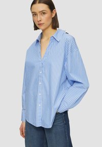 Lichtblauwe overhemd met witte verticale strepen, losse pasvorm, lange mouwen en een brede kraag. Draag het met donkerblauwe jeans.