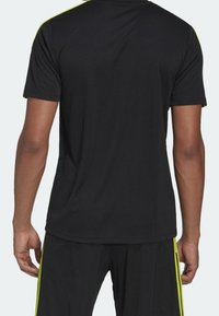 Svart atletisk t-shirt med korta ärmar, som har neon gula detaljer på axlarna, mjukt tyg och en avslappnad passform.