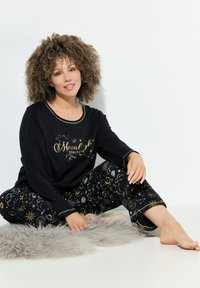 Černý pyžamový top s dlouhým rukávem a zlatým potiskem, párovaný s černými kalhotami s nebeskými vzory v různých barvách. Měkká textura.