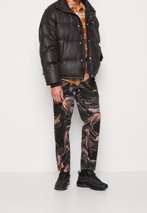 Person wearing a black puffer jacket, orange plaid shirt, black sneakers, and black pants with orange and purple abstract swirl patterns.