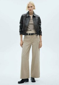 Black leather bomber jacket, striped beige top, beige wide-leg trousers, black belt, and ankle boots. Neutral colors and textured materials.