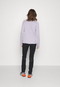 Camisa de manga larga de color púrpura claro con tejido texturizado, combinada con pantalones negros de diseño elegante y zapatos gris-naranja con detalles.