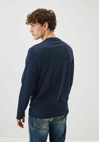 Camicetta a maniche lunghe blu navy in tessuto morbido, caratterizzata da una vestibilità rilassata e scollatura rotonda, abbinata a jeans blu sbiaditi.