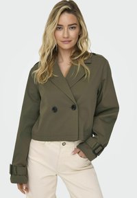Geknipte olijfgroene dubbel button-up jas met zwarte knopen, brede revers en bandaccenten op de mouwen; gladde textuur.
