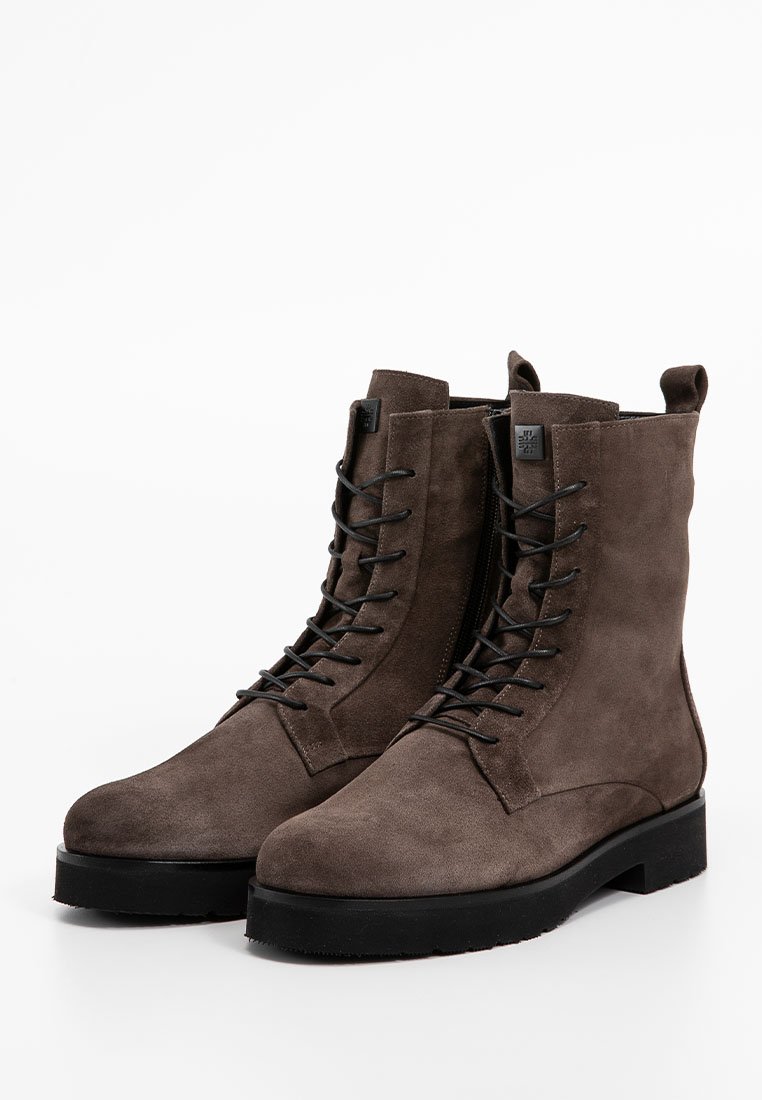 Bottines en daim marron avec un design à lacets, semelle plate noire et talon renforcé. Caractéristiques d'une texture lisse et de peu d'accents métalliques.