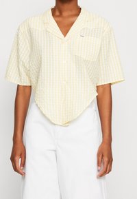 Chemise à manches courtes en vichy jaune avec col pointu, fermeture à boutons à l'avant et poche sur la poitrine gauche ; ourlet incurvé ; fabriquée dans un tissu léger.