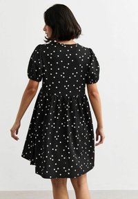 Abito nero con pois bianchi, maniche corte a sbuffo, tessuto testurizzato e gonna a ruota. I pois bianchi contrastano con lo sfondo scuro.