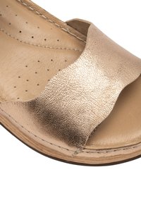 Sandal in pelle bronzo metallico con punta aperta, cinturino curvo e superficie testurizzata. Soletta leggermente imbottita con piccole perforazioni.
