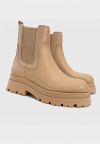 Bottines beiges à chevilles avec panneaux latéraux élastiques, en cuir lisse, semelles épaisses et motifs rainurés pour une meilleure adhérence. Design moderne et épuré.