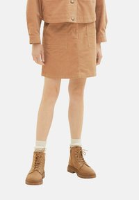 Jupe mini en velours côtelé brun avec poches latérales, associée à des bottines à lacets beige et des chaussettes en laine crème. Fini en tissu simple et texturé.