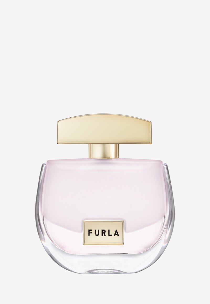 Transparante gebogen glazen parfumfles met lichtroze vloeistof, gouden rechthoekig etiket "FURLA" en brede gouden dop op witte achtergrond.