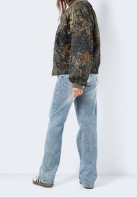 Kurtka bomber w kamuflażu w ciemnozielonym i pomarańczowym kolorze z elastycznymi mankietami, zestawiona z jasnoniebieskimi dżinsami o prostym kroju i casualowym obuwiem.