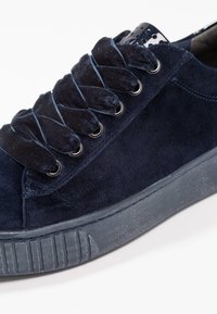 Námořnické semišové tenisky s kulatými šňůrkami, kovovými kovovými očka a strukturovanou šedou gumovou podrážkou. Hladký povrch a jemný lesk s polstrovacími detaily.