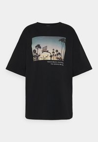 Czarny t-shirt z krótkim rękawem i luźnym krojem. Na przednim panelu grafika przedstawia zachód słońca z palmami, koszem do koszykówki oraz tekst poniżej.