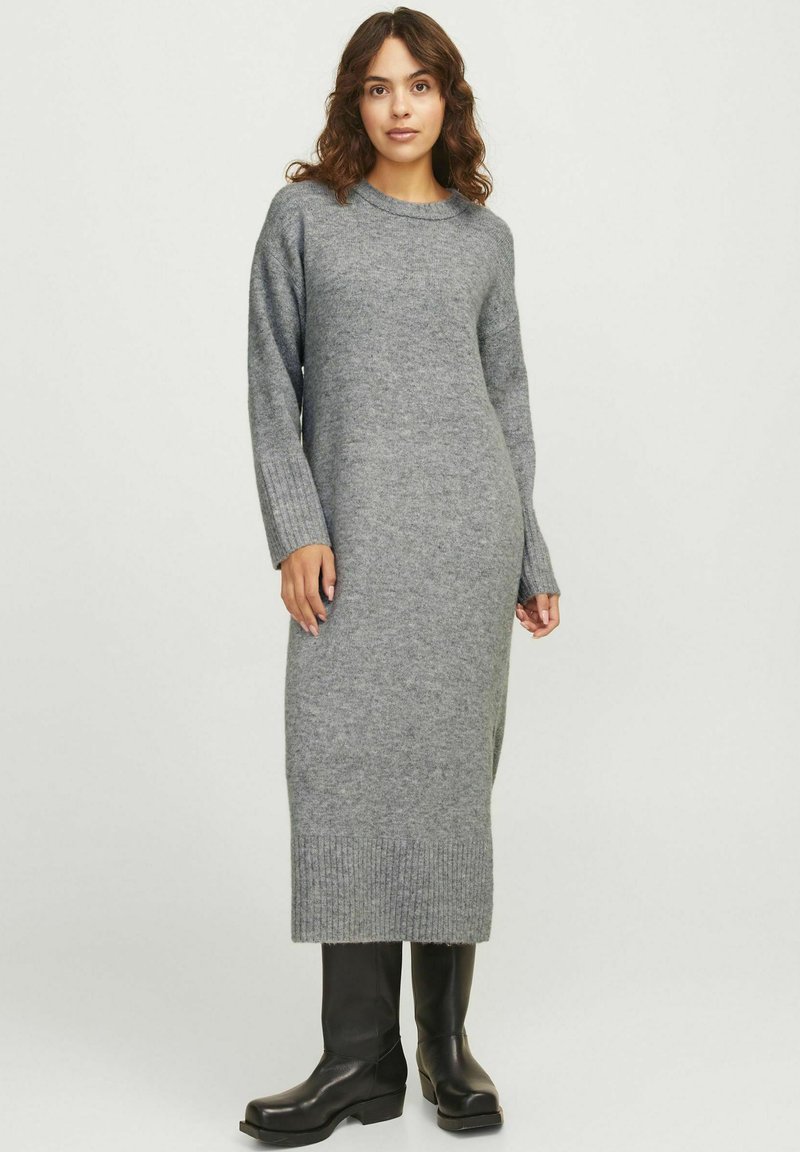 Pilkas megztas suknelė su apvalia iškirpte, ilgomis rankovėmis ir raštuotais rankogaliais. Ji siekia vidurį blauzdų ir turi prigludusią siluetą. Juodi bateliai iki kelių.