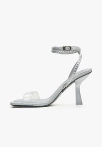 Duidelijke haksandalen met een open teen en enkelband, met zilveren studs langs de banden en hak. Transparant bovendeel.