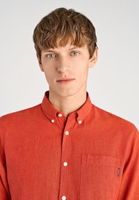 Czerwona koszula z guzikami, wyposażona w kieszonkę i subtelny wzór. Wykonana z lekkiego materiału z kołnierzykiem, prezentująca czysty, klasyczny design.