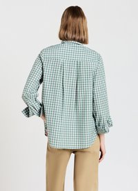Green and white checked shirt with long sleeves, rounded hem, and back pleat detail. Made of lightweight fabric, features roll-up sleeves.