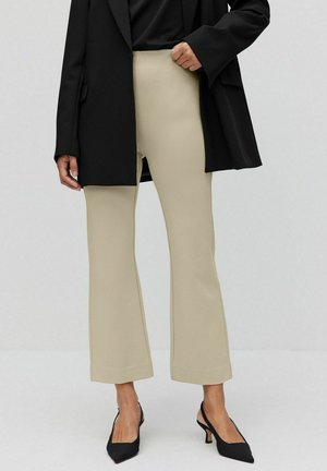Beige utsvängda byxor i stretchy material med hög midja och sömdetaljer, samt en svart överstor blazer och svarta klackar.