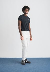 Juoda trumpomis rankovėmis marškinėliai su logotipu, balti sportinės kelnės ir juodi sportbačiai. Paprastas dizainas, lengva medžiaga ir laisvas prigludimas. Tekstūruoti raštai ant odos.