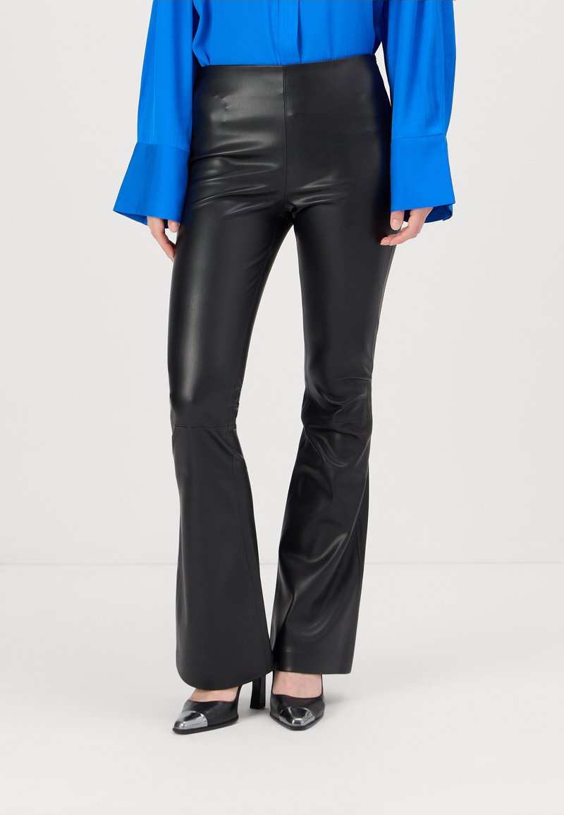 Schwarze Kunstleder-Hose mit weitem Bein und hoher Taille, glatter Textur und leichtem Glanz. Getragen mit einer blauen Bluse und schwarzen High Heels.